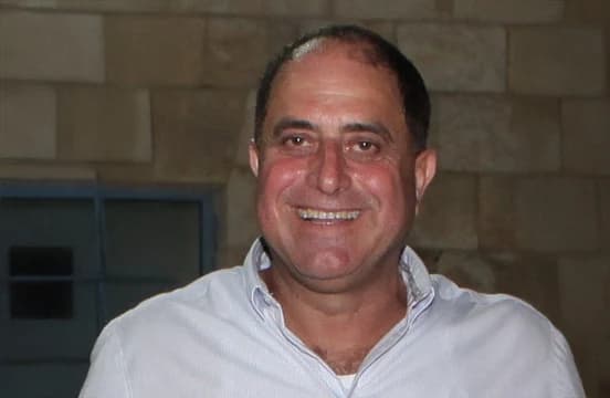 بقميص أزرق فاتح، مصوَّر أمام جدار حجري ونافذة ذات قضبان.