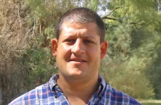 بقميص مربعات أزرق وأحمر، مصوَّر في الخارج وخلفه أشجار.